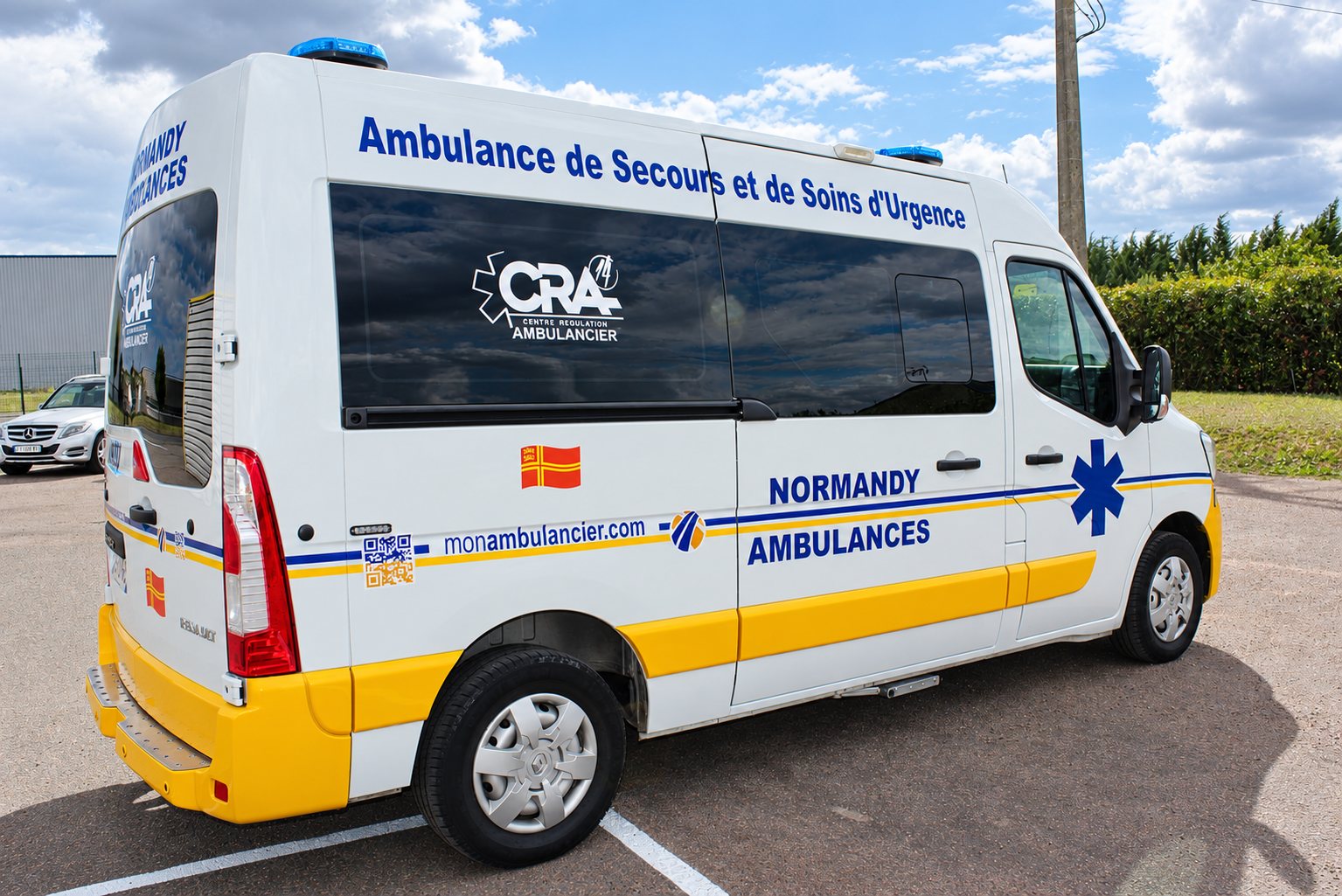 Ambulance Normandy Ambulances blanche et jaune vue de trois quarts arrière, portant l’inscription Ambulance de Secours et de Soins d’Urgence